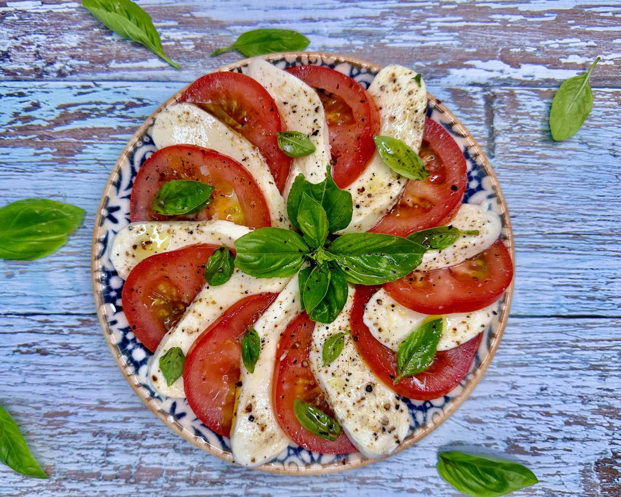 Caprese salat - tomater og mozzarella i skiver med frisk basilikum, olivenolie og friskkværnet peber.