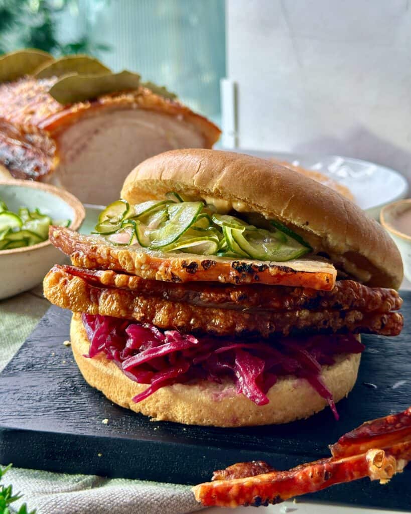 Flæskestegssandwich med flæskesteg med sprød svær, agurkesalat og hjemmelavet rødkål i blød burgerbolle.