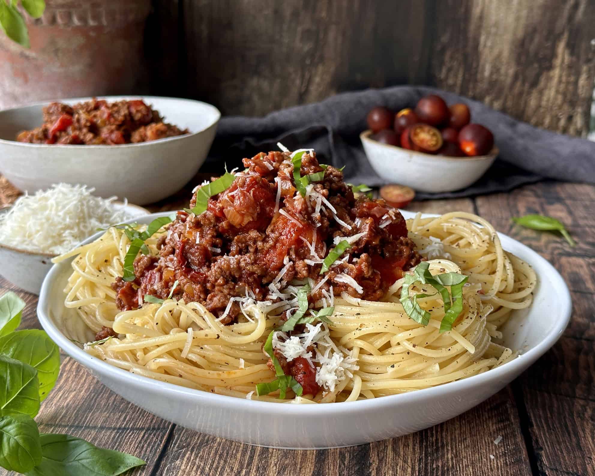 Spaghetti bolognese i skål med revet parmesan og frisk basilikum