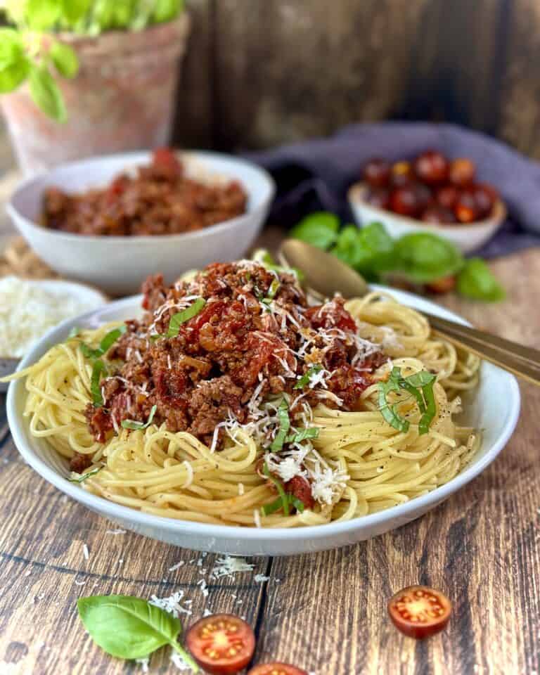 Spaghetti bolognese i skål med revet parmesan og frisk basilikum