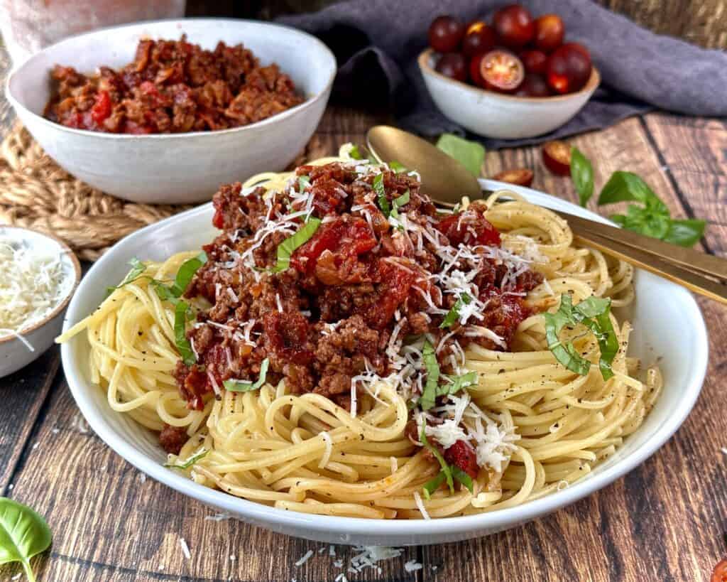 Spaghetti bolognese i skål med revet parmesan og frisk basilikum
