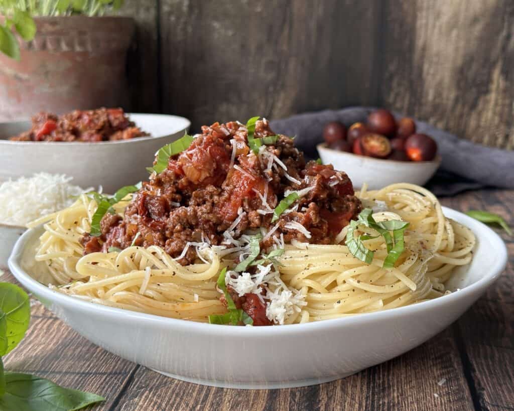 Spaghetti bolognese i skål med revet parmesan og frisk basilikum