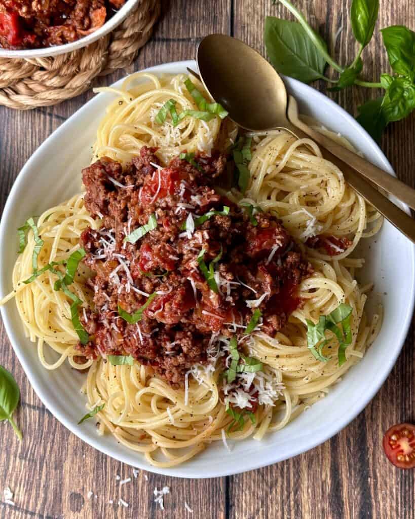 Spaghetti bolognese i skål med revet parmesan og frisk basilikum