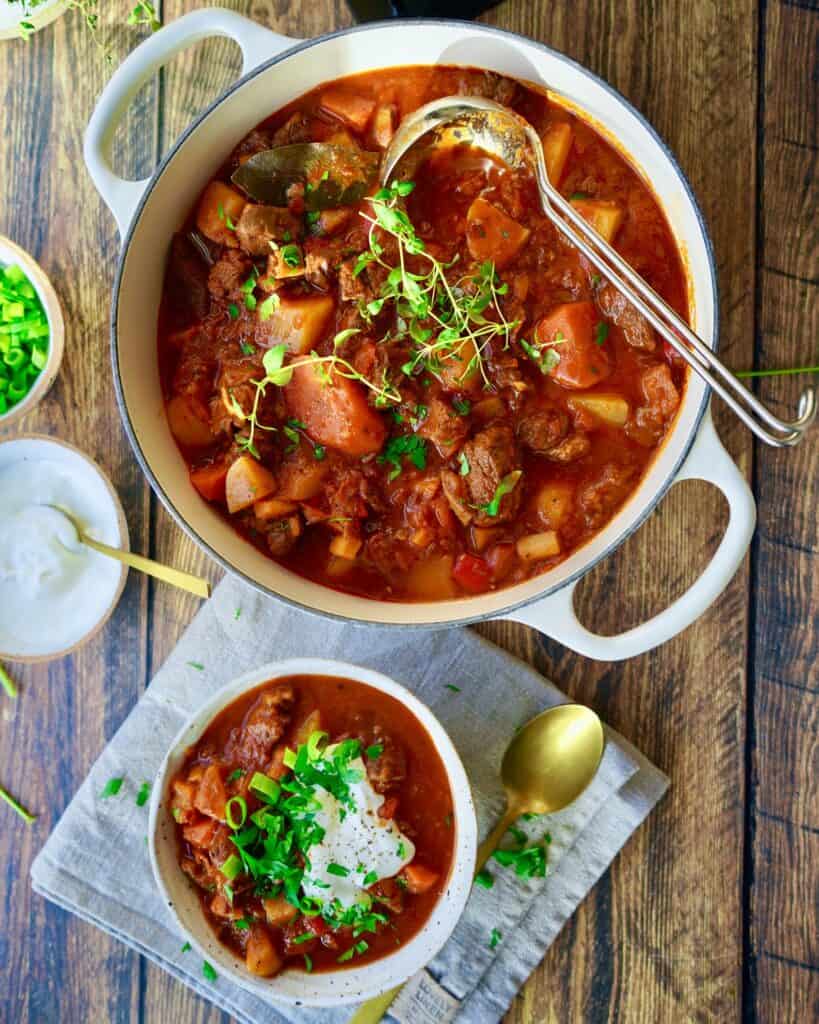 Hjemmelavet gullash suppe i gryde og med servering i skål med creme fraiche og grøn topping