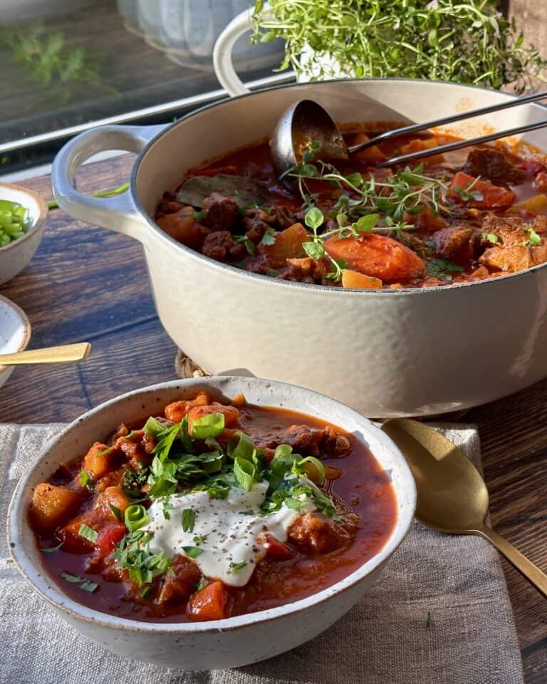 Hjemmelavet gullash suppe i gryde og med servering i skål med creme fraiche og grøn topping